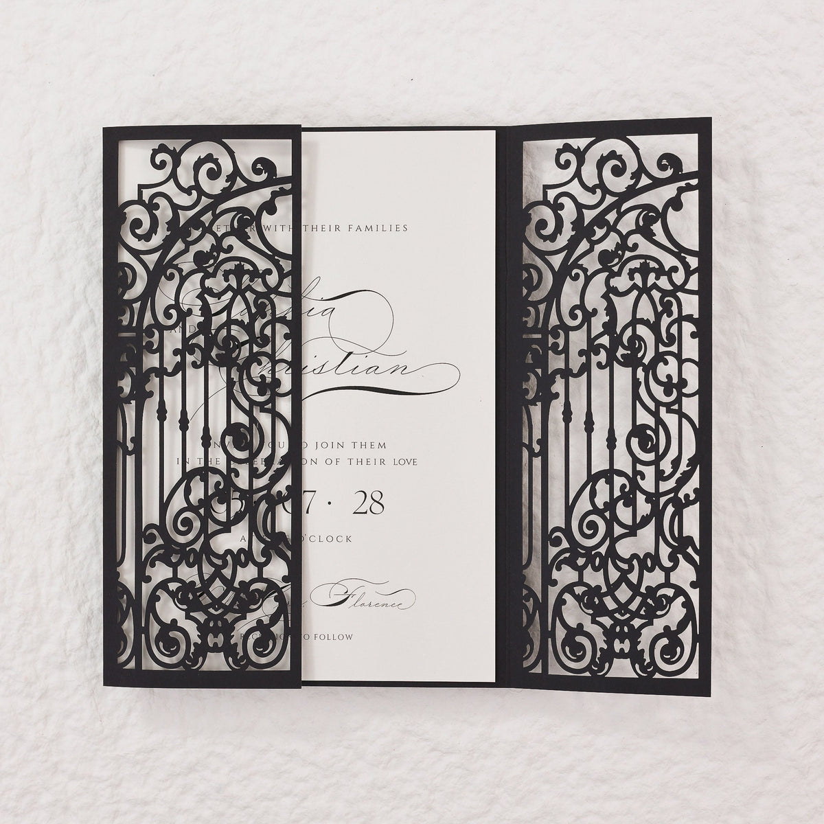 Black laser cut wedding invitation with a gate design. The invitation reads 'With their families, [Name] and [Name] join them on the celebration of their love, [Date], [Time], [Location] to follow.'