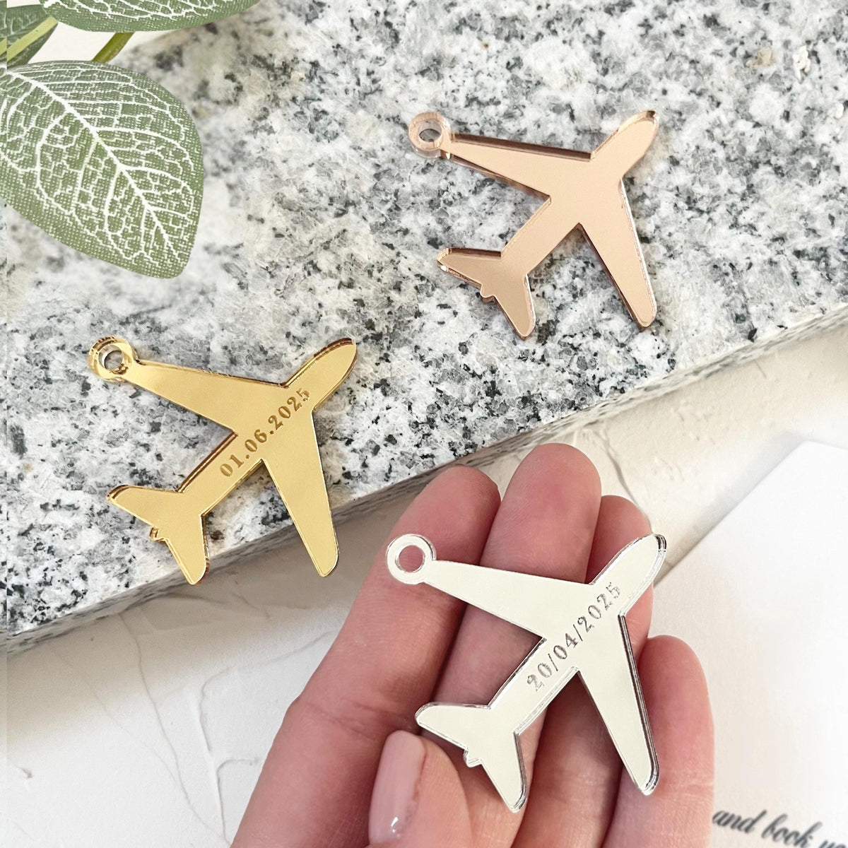 Unique airplane tags made of mirror acrylic - gold, silver and rose gold, on which the wedding date is elegantly laser engraved.   They are placed on a textured surface, and on the side lies Save the date - a passport-style invitation.