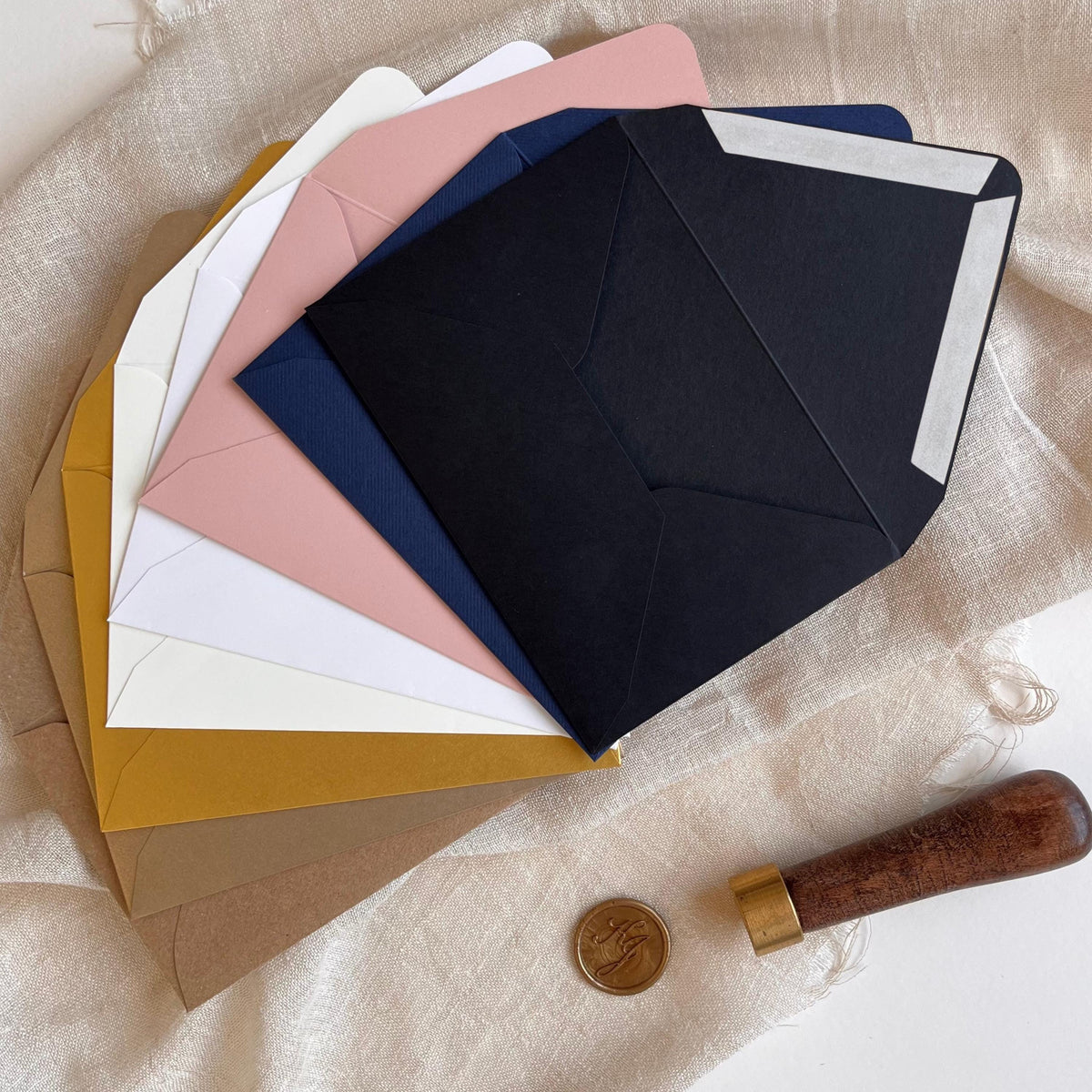 Eight standard-size RSVP envelopes displayed open in Black Matt, Navy Blue Matt, Blush Pink Matt, White Metallic, Cream Matt, Gold Metallic, Old Gold Metallic, and Eco Matt, featuring a convenient ribbon closure for easy opening and resealing.